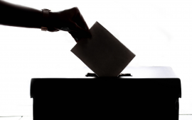 Black and White image of hand dropping ballot into box