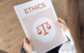 A  person holding a bound document with the title "Ethics" and an image of a weighing scale.